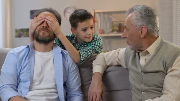 Hijo cerrando ojos de padres, abuelo dando caja de regalo, sorpresa de cumpleaños, familia — Vídeos de Stock