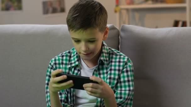 男孩在家里的智能手机上玩电子游戏, 年轻时的小玩意成瘾 — 图库视频影像