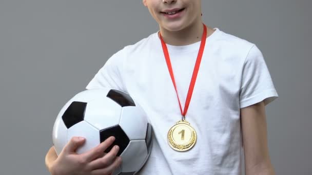 Хлопчик з футбольним м'ячем і перше місце медаль, що стоїть на сірому фоні — стокове відео