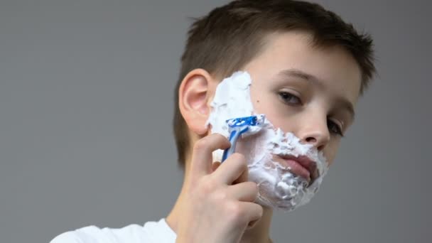 Chłopiec z pianką na twarzy golenia przed lustrem, symulując zwyczaj ojców — Wideo stockowe