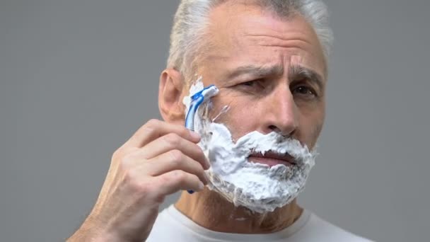 Літній чоловік з піною на обличчі голиться борода, готується до побачення, гігієна — стокове відео