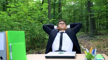 Onun iş bitirme ve yeşil orman sandalyede rahatlatıcı mutlu genç işadamı