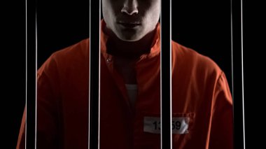 Criminal in orange uniform behind prison bars, serving life sentence for murder clipart