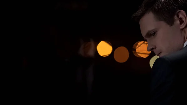 Man in suit thinking serious decisions at night, city lights on background