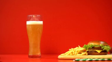 Köpük ve hamburger kırmızı arka plan, karbonhidratlar ve yağlı gıdalar ile bira