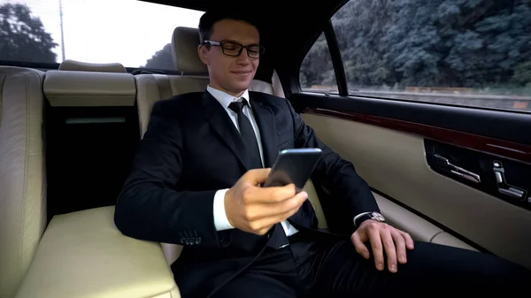 電話アプリケーションを使用して高価な車の後部座席に乗って喜んでビジネスマン — ストック写真