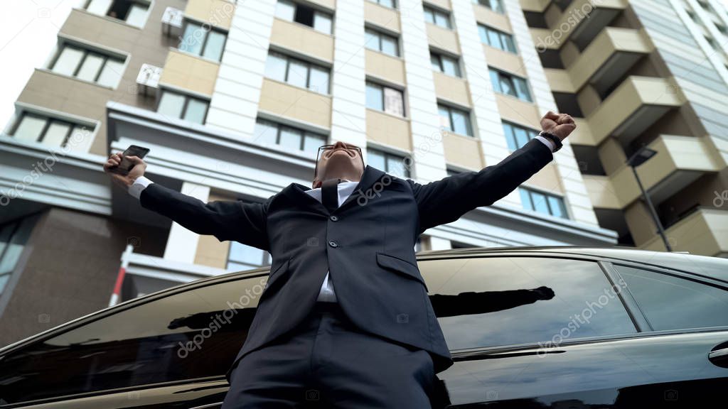 Extremely happy businessman spreading arms, lottery winner of flat and car
