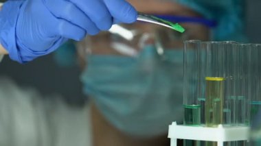 Güvenlik gözlüklerini test tüpüne reaktif ekleyerek, reaksiyonu gözlemleyen araştırmacı