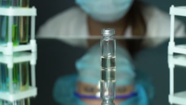 Лаборант рассматривает образец вакцины, стоящей на столе, разработку лекарств — стоковое видео