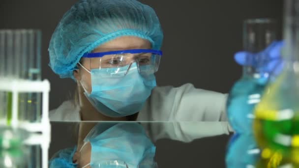 Cientista em uniforme de proteção olhando para o líquido azul em frasco, análise de água — Vídeo de Stock