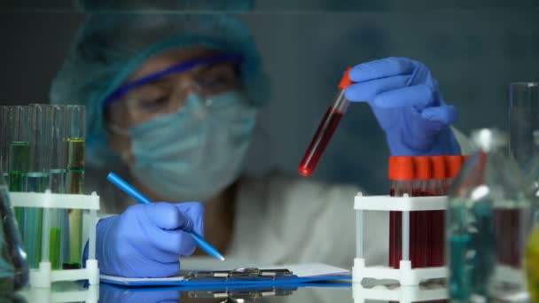 Ученый проверяет трубки с анализом крови и делает заметки, вспышка эпидемии — стоковое видео