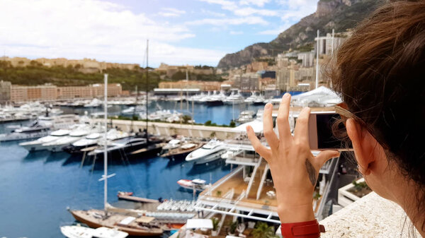 Tourist girl taking photo of yachts in Mediterranean sea port, using smartphone