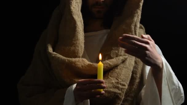 Jesus Cristo de roupão segurando vela acesa contra fundo escuro, luz — Vídeo de Stock