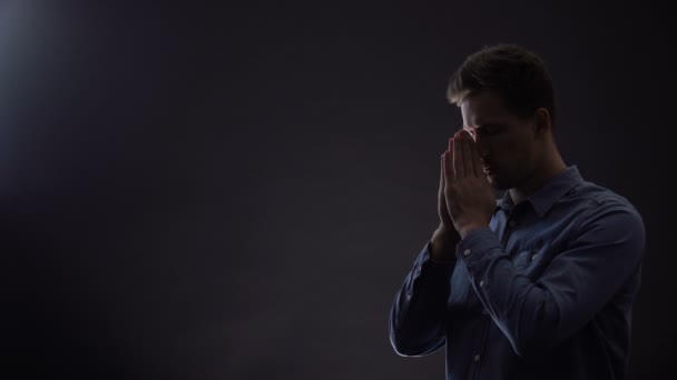 Νέος άνθρωπος προσεύχεται στο σκοτεινό δωμάτιο κάτω από ευλογημένο φως από τον ουρανό, Χριστιανισμός — Αρχείο Βίντεο