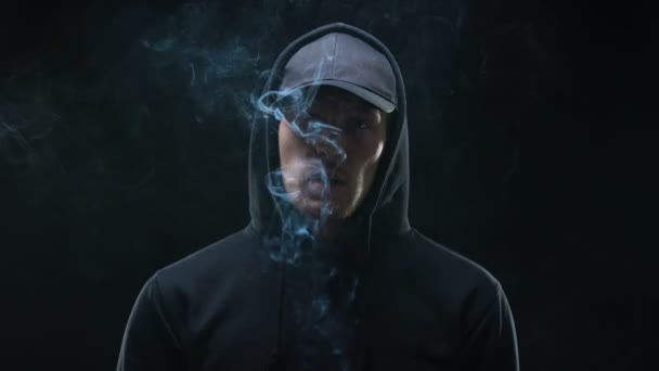 Intimidation masculine en sweat à capuche fumant la cigarette sur fond sombre, criminel de nuit — Video