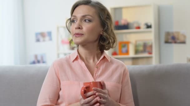 Одинокая грустная женщина пьет чай на диване, обдумывая решение жизненных трудностей — стоковое видео