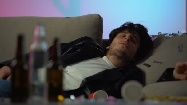 Сонный пьяница с головной болью после вечеринки дома, пустые бутылки на столе — стоковое видео