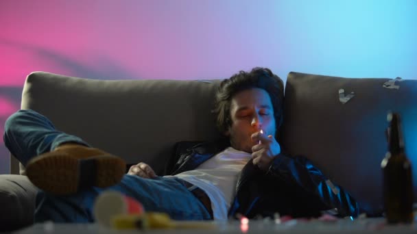Homem bêbado acendendo cigarro, fumando e relaxando no sofá na festa da boate — Vídeo de Stock