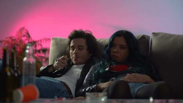 Ζευγάρι των μεθυσμένων νέοι άνθρωποι καθισμένοι χαλαροί στην ακατάστατο δωμάτιο, νύχτα κόμμα — Αρχείο Βίντεο