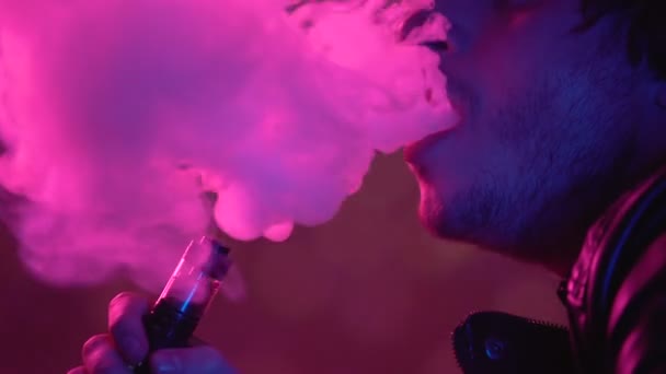 Man vaping e-cigarette in darkness, exhaling clouds of smoke, unhealthy habit — Stock Video
