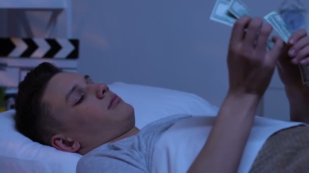Подросток считает доллары, прячет банкноты под подушкой, экономит карманные деньги — стоковое видео