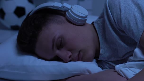 Hombre adolescente en auriculares durmiendo en casa, escuchando audiolibros, estudiando — Vídeos de Stock