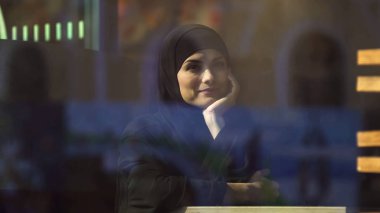 Sipariş için bekleyen hijab giyen kafede oturan güzel düşünceli Müslüman Bayan