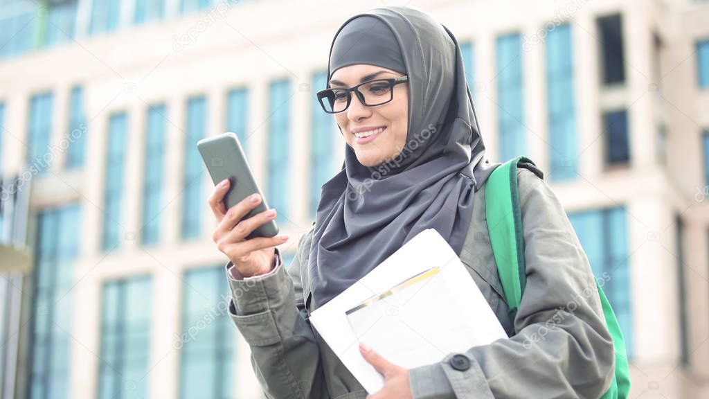 Happy Muslim woman student chatting on phone outdoors on university campus