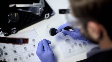 Private detective using powder and brush to take fingerprint from piece of glass clipart