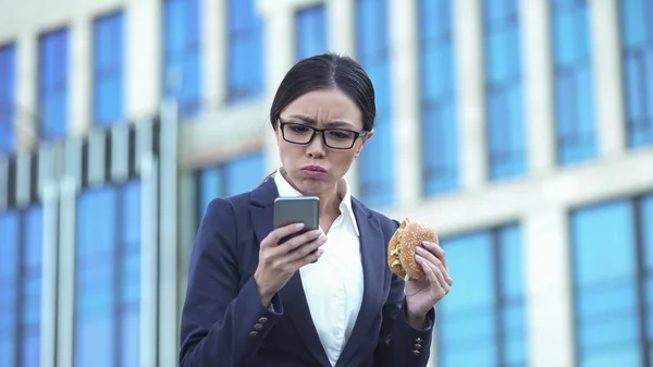 Kvinnliga Kontorschef Äta Ohälsosam Burger Kontrollera Meddelanden Telefon Stress — Stockfoto