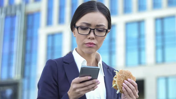 Överarbetade Kvinnlig Anställd Läsa Business Nyheter Hålla Burger Lunchtid — Stockfoto