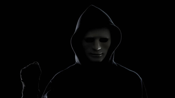 Maniac in white mask and hoodie showing fist, isolated on black background