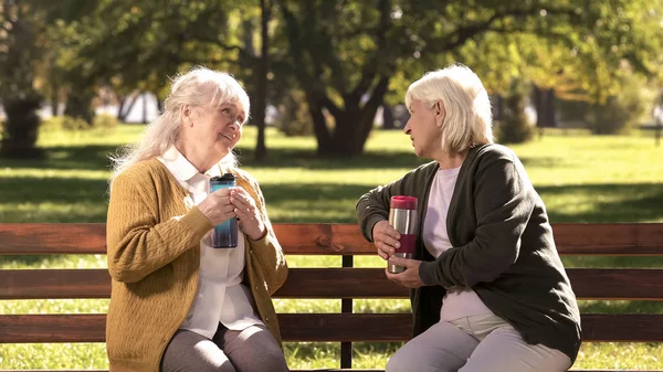 Dos Ancianas Bebiendo Caliente Tazas Viaje Sentadas Banco Soleado Parque —  Fotos de Stock