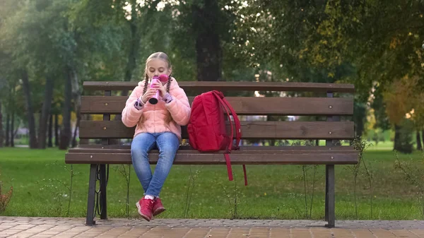 愉快的女学生与背包喝茶从热水瓶杯子作为坐在长凳上 — 图库照片