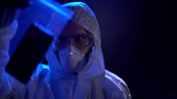 Криминалист держит мобильник в прозрачной упаковке, улики на месте преступления
