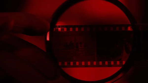 Photographer looking at camera roll through magnifying glass, red light room