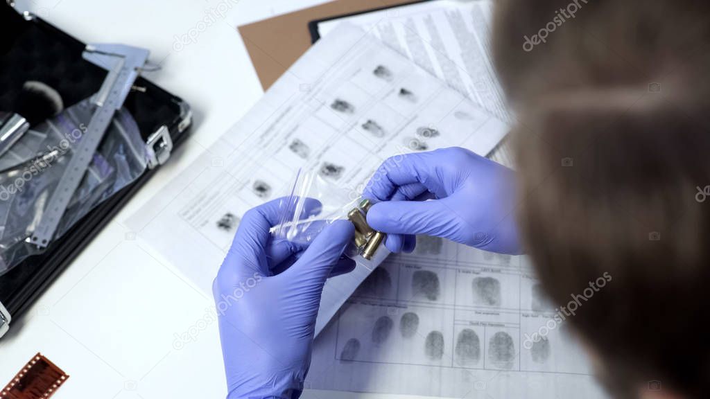 Male detective wearing gloves examining bullets from crime scene in office