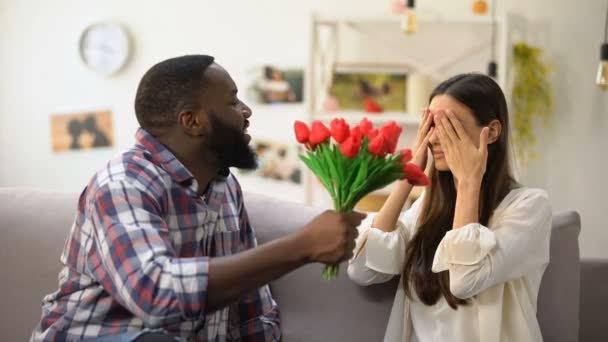 Hombre afroamericano presentando manojo de tulipanes a chica caucásica, regalo de aniversario — Vídeo de stock