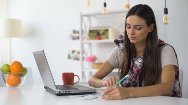 Young woman with laptop and bills counting incomes and expenses, home budget