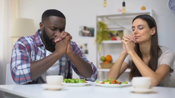 Jeune couple mixte priant avant le déjeuner, salade végétarienne saine sur la table — Video