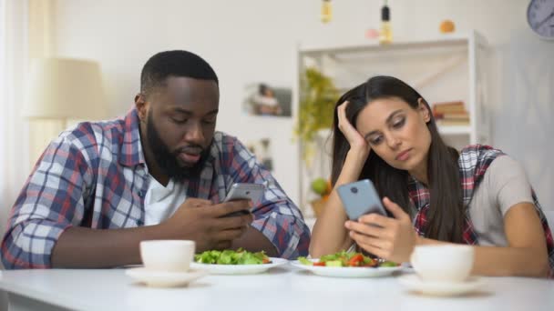 Оскорбленная пара смешанной расы, использующая смартфоны во время обеда, недоразумение — стоковое видео