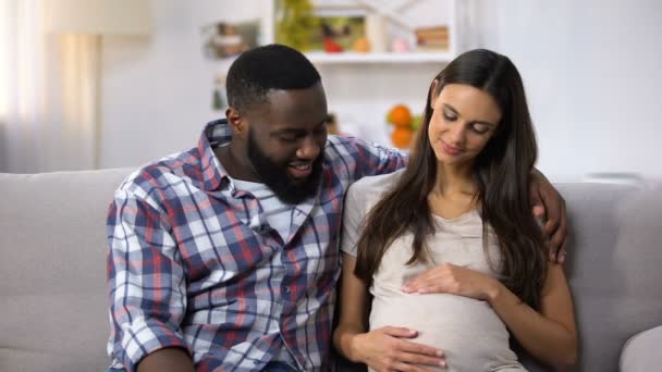 Familia mixta mirando a la cámara, mujer embarazada sosteniendo la barriga, felicidad — Vídeo de stock