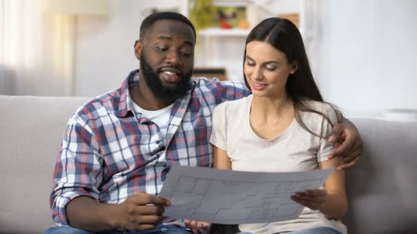 Familia multirracial joven mirando el plan de construcción, eligiendo el diseño de interiores — Vídeo de stock