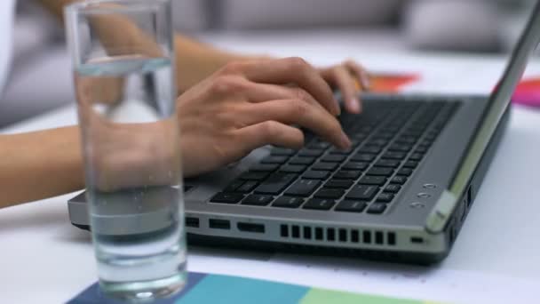 Жіночий фрілансер, що працює ноутбук крупним планом, склянка води на столі, журналіст — стокове відео