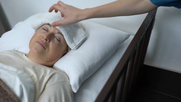 Médico tomando compresa de la frente de pacientes mayores, apoyando a la mujer enferma — Vídeos de Stock