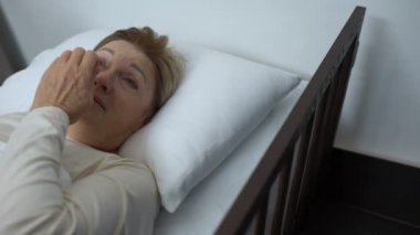 Depresyona girmiş yaşlı hasta, hasta yatağında yatan gözyaşlarını silerek, gönüllüyü destekleyen Bayan