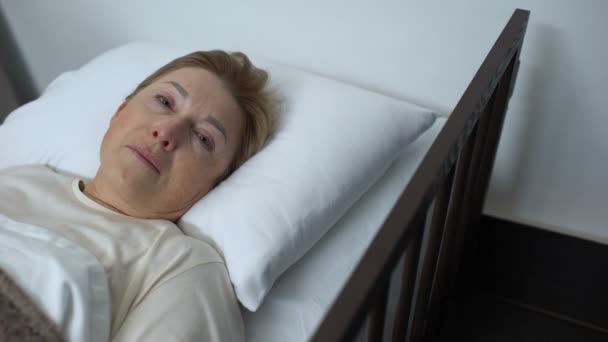 Terminaal zieke Senior dame huilen en op zoek naar camera, liggend in hospice bed — Stockvideo