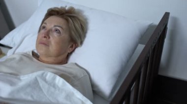 Hasta yatakta yatan ve etrafına bakan endişeli yaşlı hasta, Alzheimer hastalığı