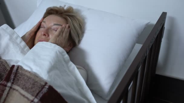 Paciente anciana masajeando templos, sufriendo terrible migraña en cama enferma — Vídeos de Stock