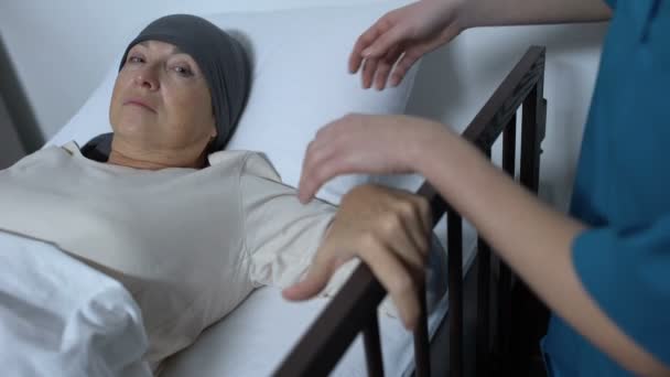 Онколог помогает пожилой пациентке встать с больничной койки, оказывает медицинскую поддержку — стоковое видео
